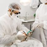 From above of unrecognizable male stomatologist and female assistant in uniforms treating patient teeth in clinic